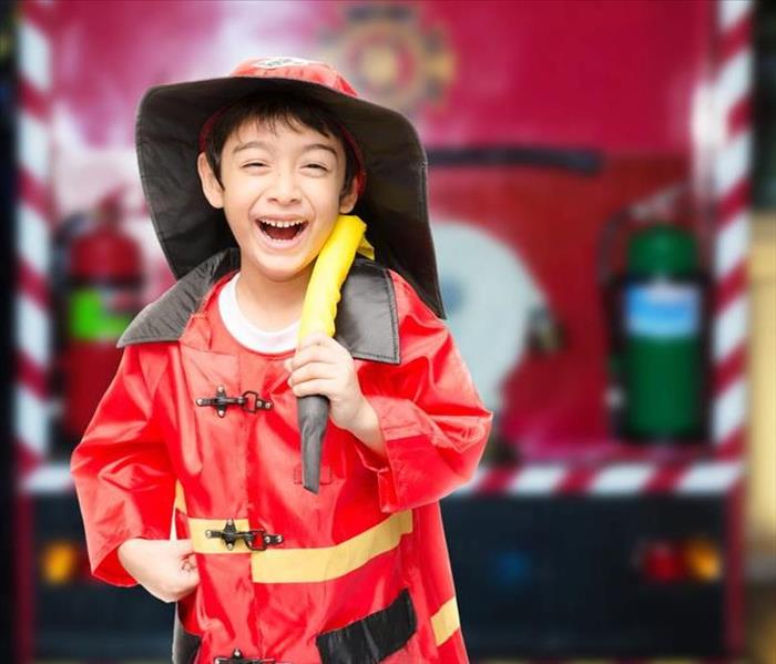 Little boy dressed as a firefighter and holding a hose over his shoulder